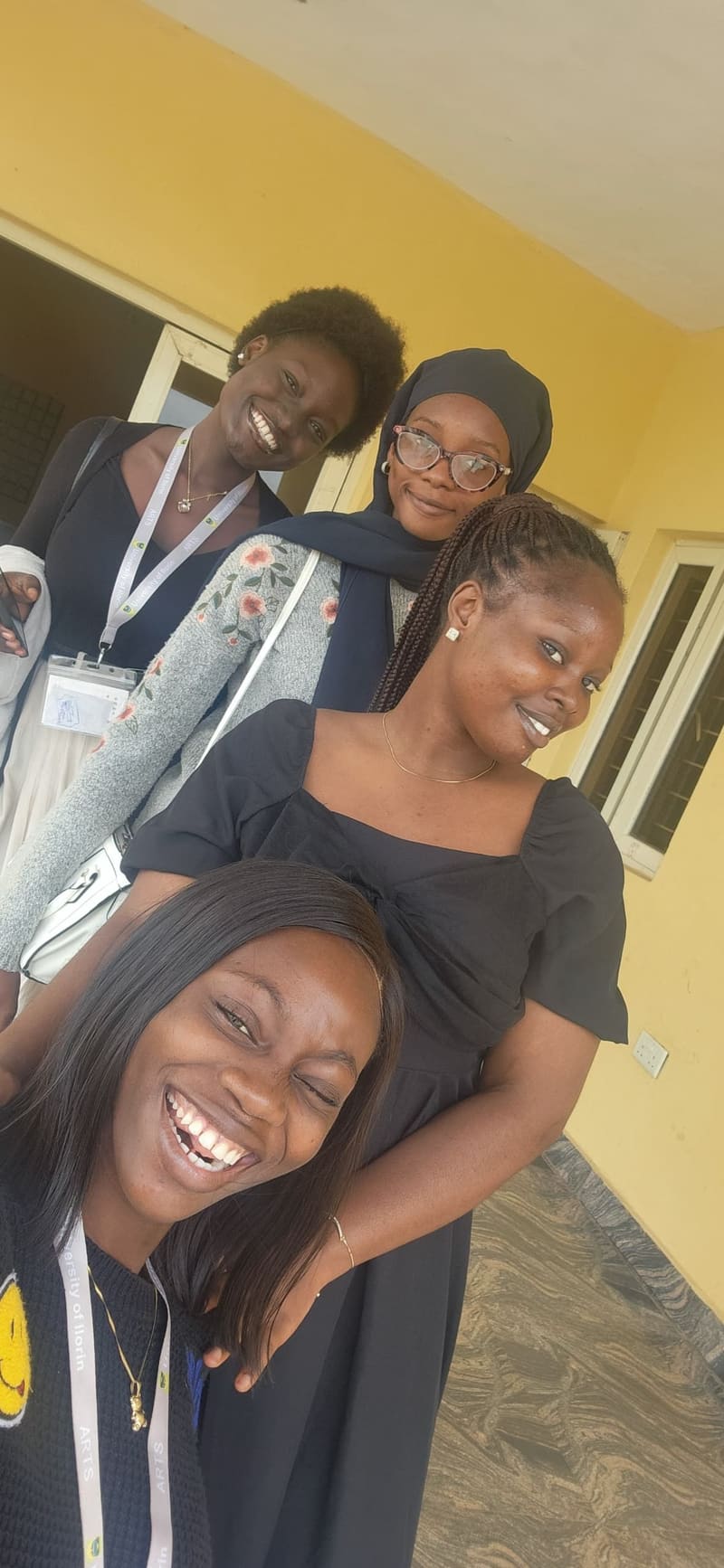 Four friends with lanyards squeezed into one selfie against a yellow wall