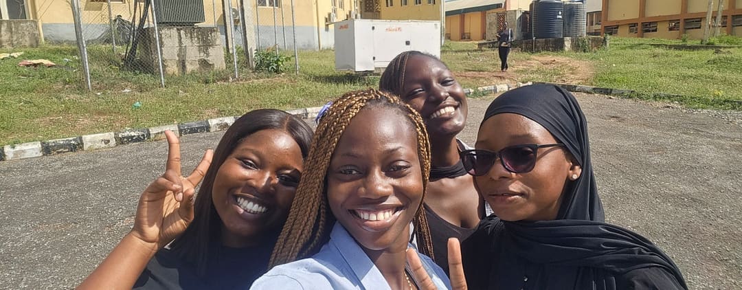 Four friends smiling in a selfie with a yellow building behind them
